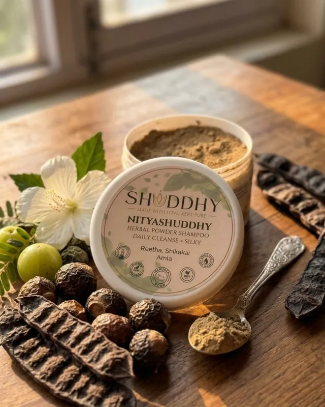 Open NITYASHUDDHY jar with light brown herbal blend and a spoon beside reetha, shikakai pods and amla